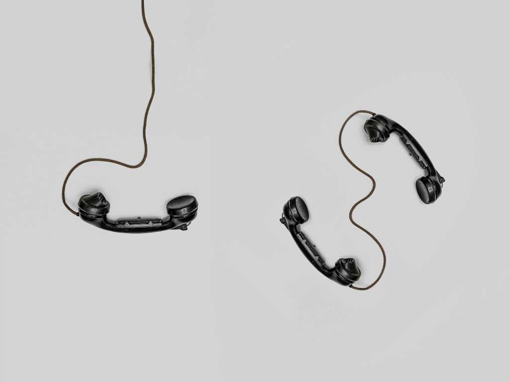 Two vintage black telephone handsets connected by cords on gray background.